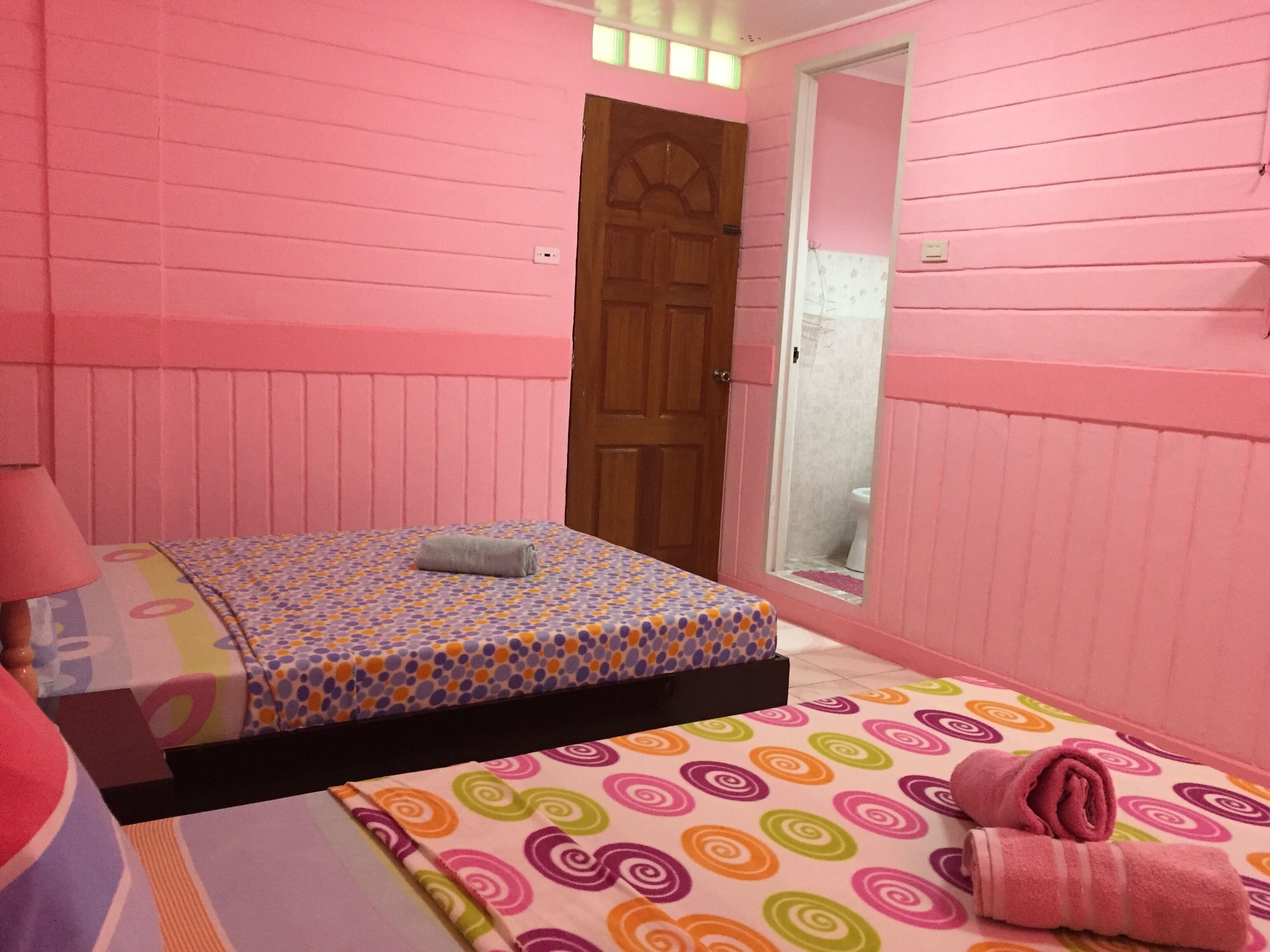 A pink-themed room with a bed, a wooden door, and a window.