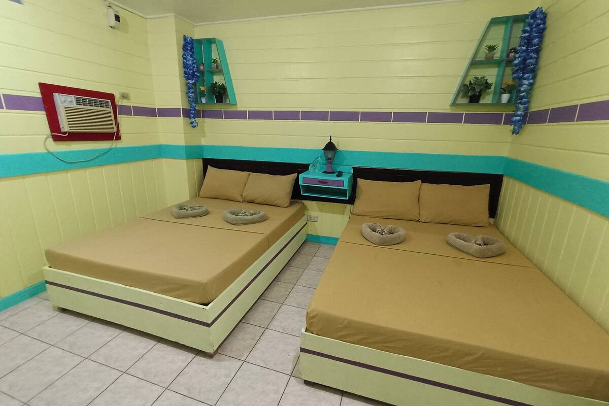 A room with two beds, a small table with a lamp, and a mirror on the wall.