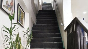 A staircase with black steps leading to an upper floor, flanked by potted plants and framed artwork. - Hayward Travel Inn (Tacloban)