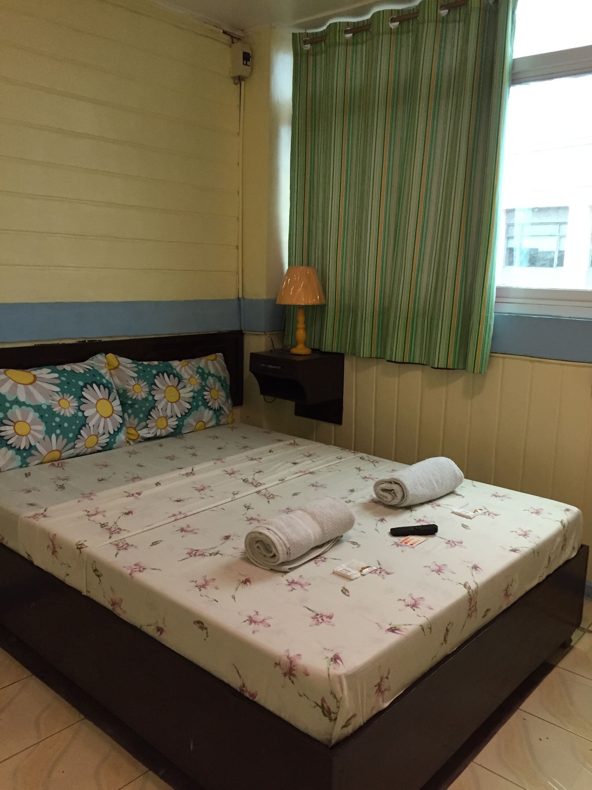 Una cama individual con ropa de cama floral, una lámpara de noche y un control remoto sobre la cama.