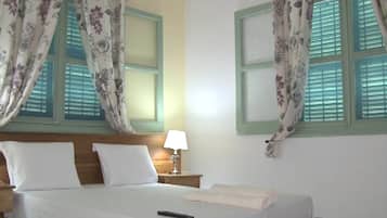A neatly made bed with white linens, a remote control on the bed, and floral curtains on the windows.