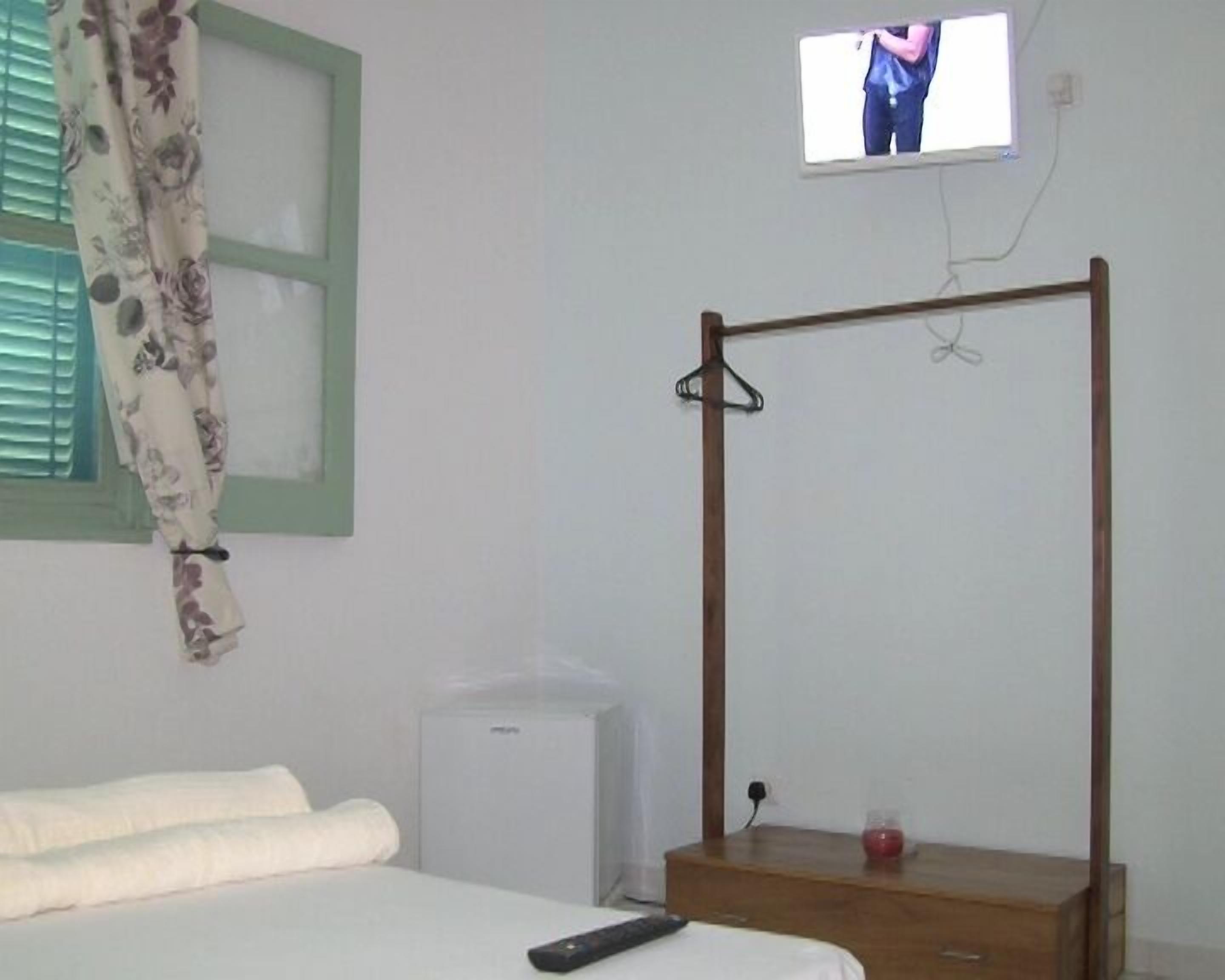 A bedroom with a bed, a bedside table, a TV mounted on the wall, and a window with curtains.