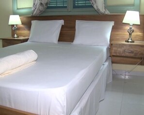 Una cama bien hecha con sábanas blancas, dos mesitas de noche con lámparas y un cabecero de madera.