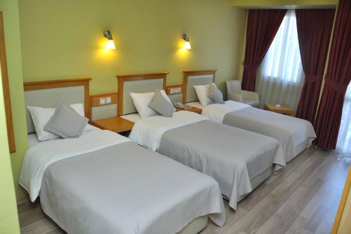 A hotel room with four single beds, a small table, and two wall-mounted lamps.