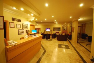 A reception area with a wooden reception desk, a television, framed pictures on the wall, and a carpeted floor.