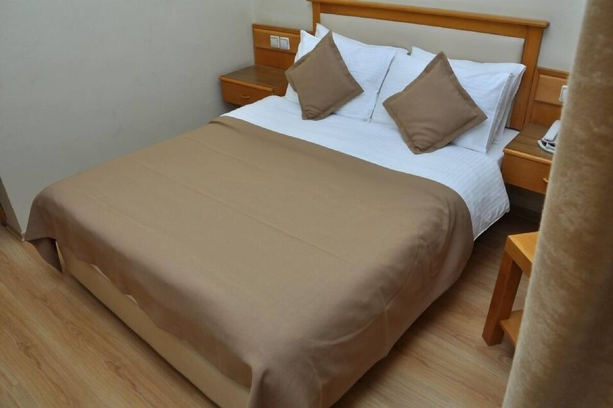 A neatly made bed with a brown bedspread and two pillows, wooden nightstands, and a telephone on one of the nightstands.