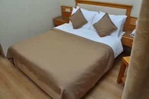 A neatly made bed with a brown bedspread and two pillows, wooden nightstands, and a telephone on one of the nightstands.