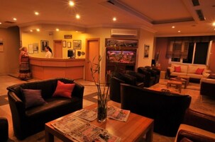 A hotel lobby with a reception desk, a fish tank, leather sofas, and a coffee table with newspapers.