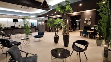 A modern lobby with seating areas, large potted plants, and a reception desk.