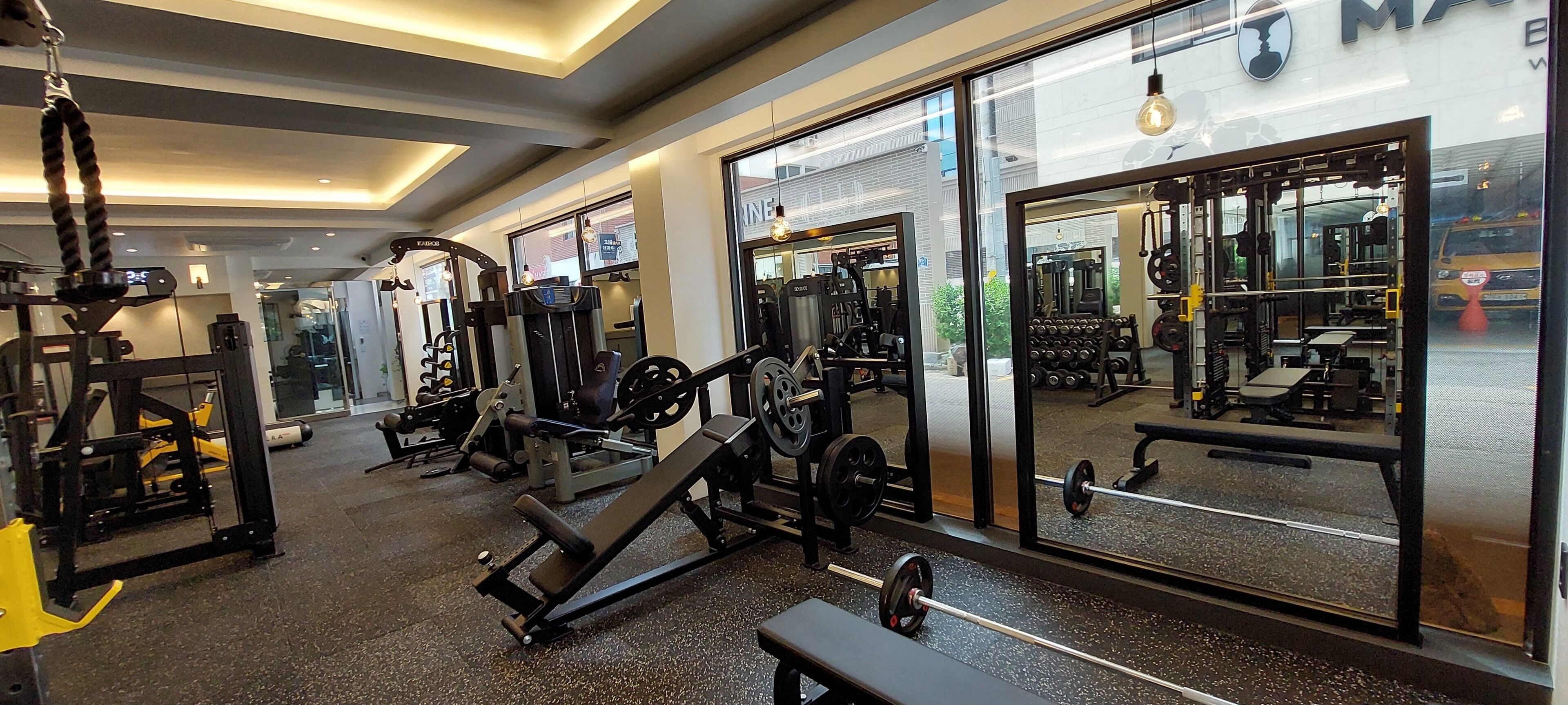 A gym with various exercise equipment, large windows, and a bench.