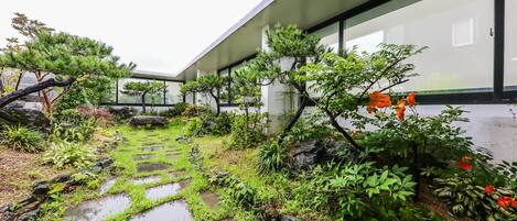 Un edificio moderno con fachada de vidrio, un camino de piedra y varias plantas y árboles.