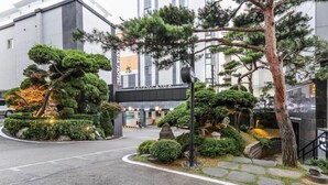 A hotel entrance with a well-maintained garden, a stone pathway, and a modern building facade.