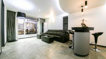 A modern living room with a sectional sofa, a coffee table, a tall column with a sculpture, and a large window with curtains.