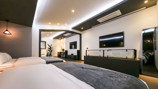 A modern hotel room with two beds, a large flat-screen TV mounted on the wall, and a built-in refrigerator.