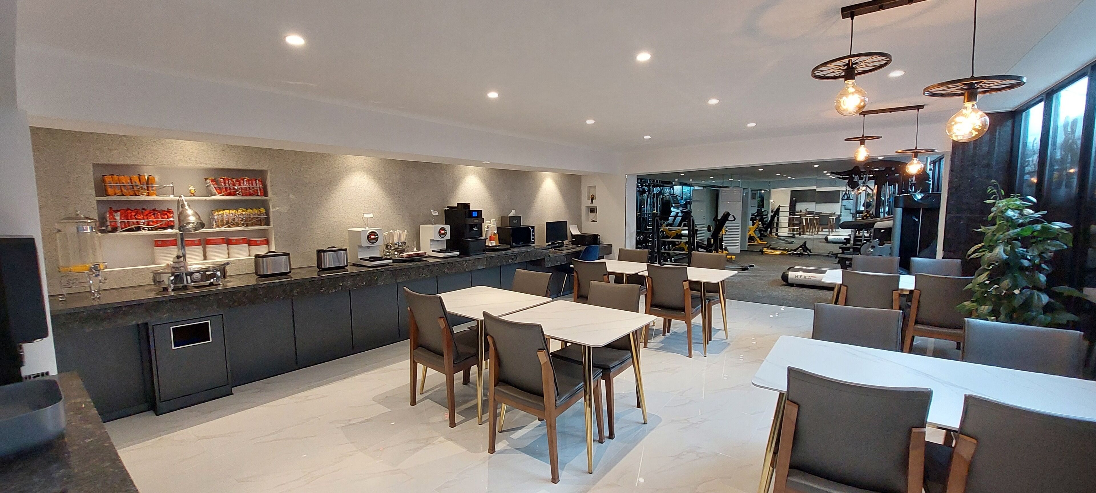 A modern kitchen with a central island, dining area with tables and chairs, and a view into a gym area.