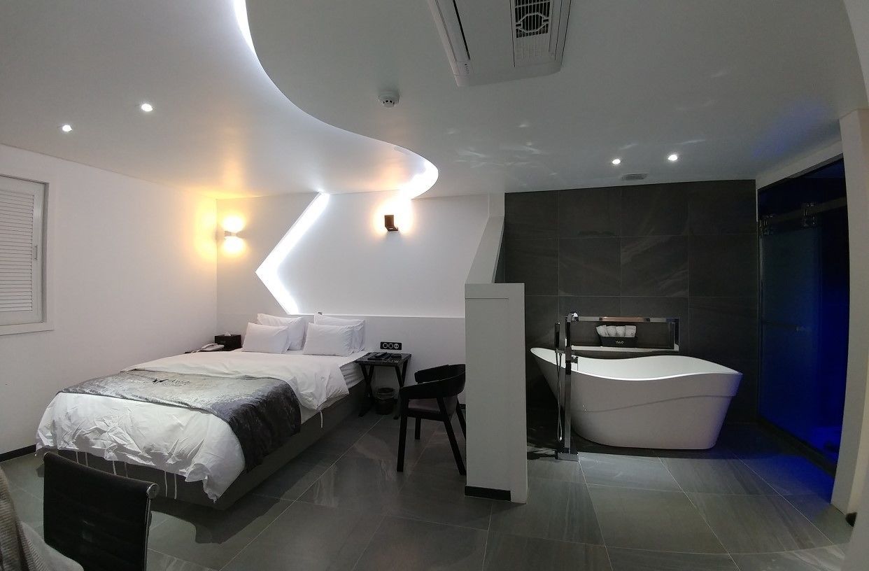 A modern hotel room with a curved ceiling, a large bed, a desk, a chair, a bathtub, and a shower.