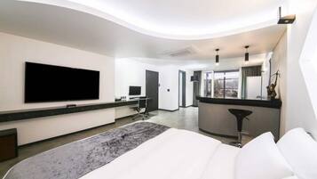 Una habitación de hotel moderna con una cama grande, un televisor de pantalla plana montado en la pared, un escritorio con una silla y vistas a la ciudad a través del ventanal.