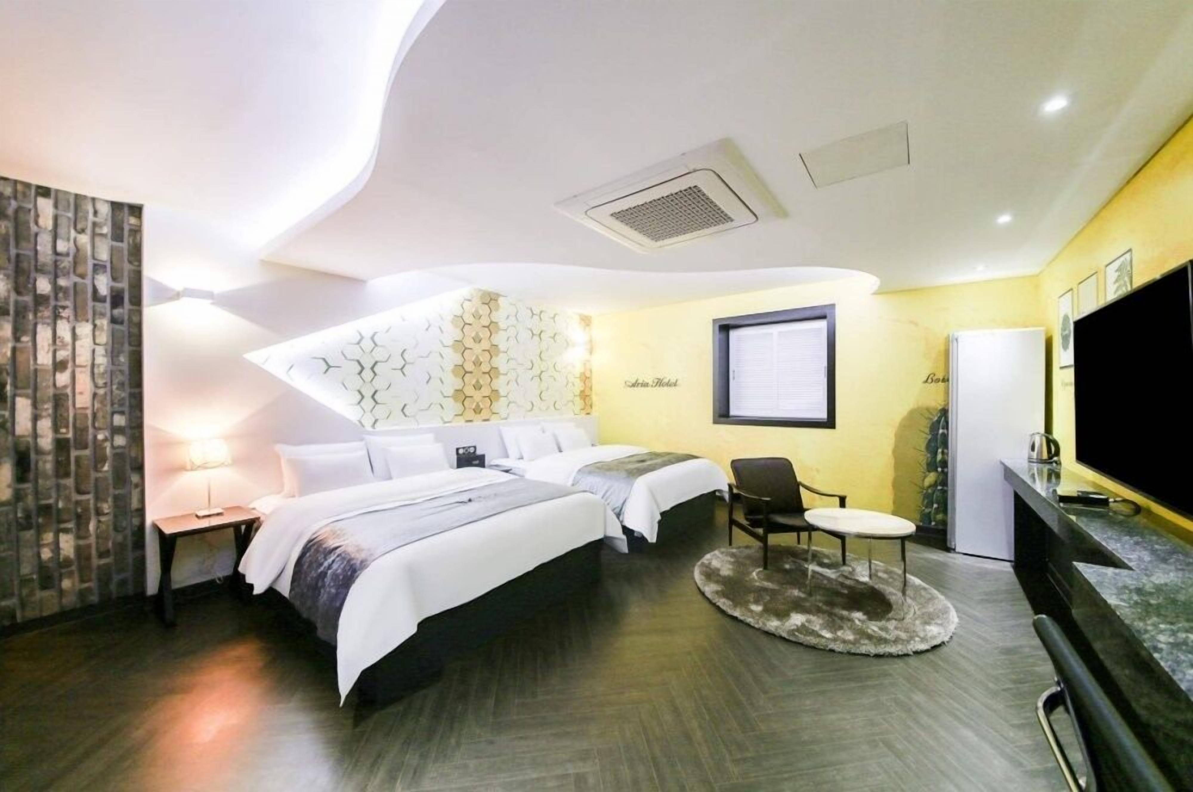 A hotel room with two beds, a TV, a desk, and a small seating area.