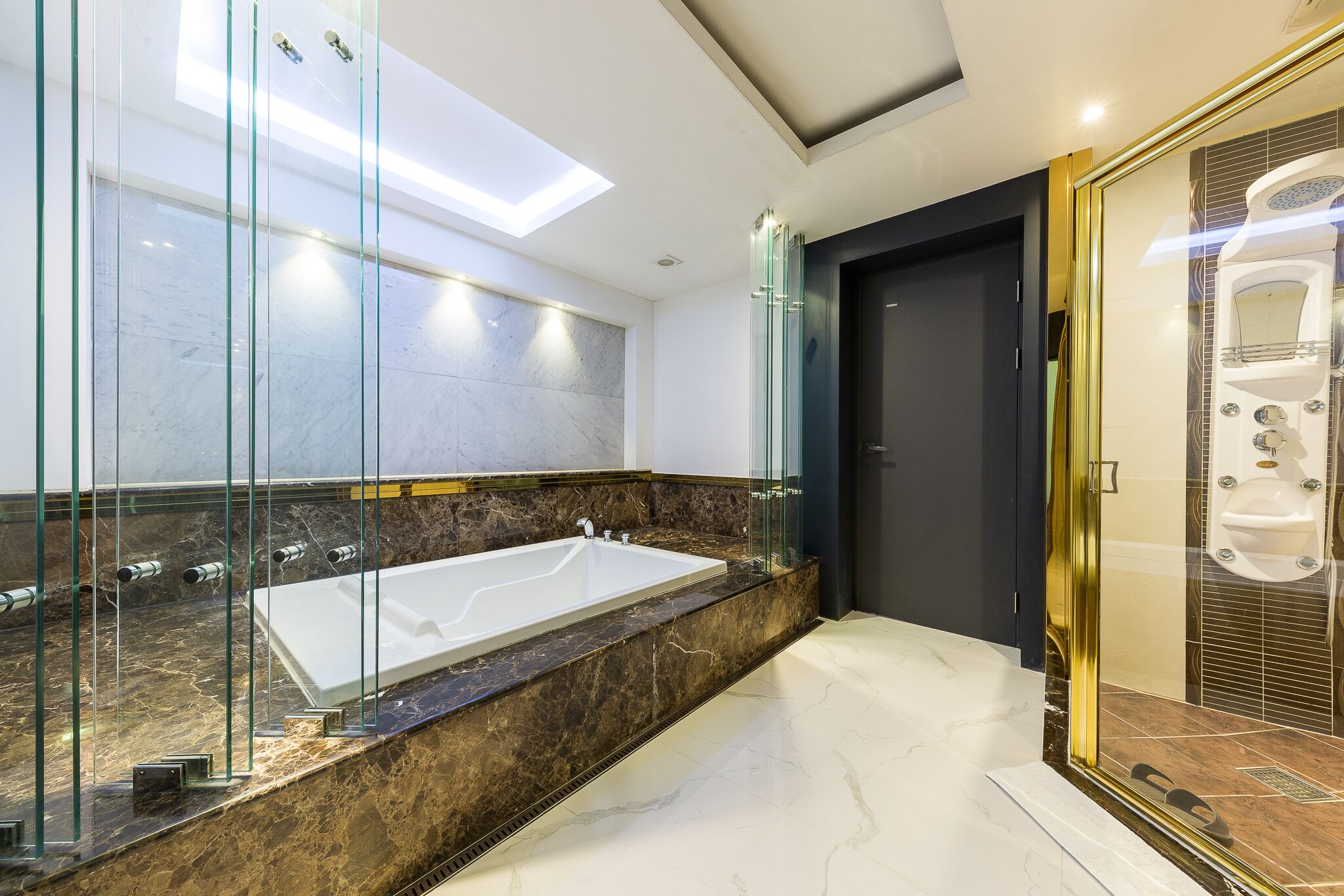 A modern bathroom with a large glass-enclosed shower, a marble vanity, and a skylight.