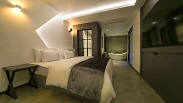 A modern hotel room with a large bed, bedside table, and a separate bathroom with a bathtub.