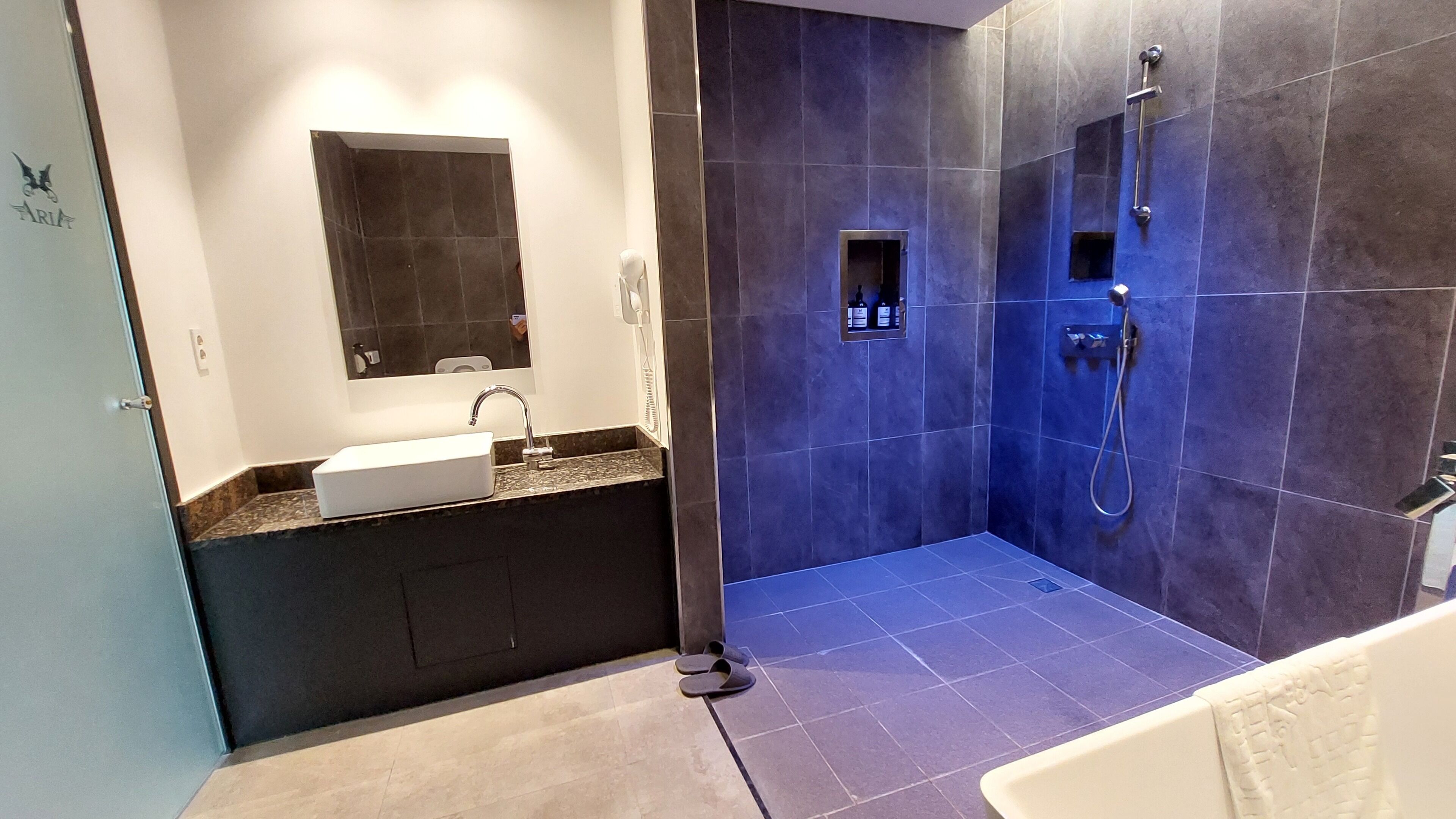 Un baño moderno con un espejo grande, un lavamanos y una zona de ducha.