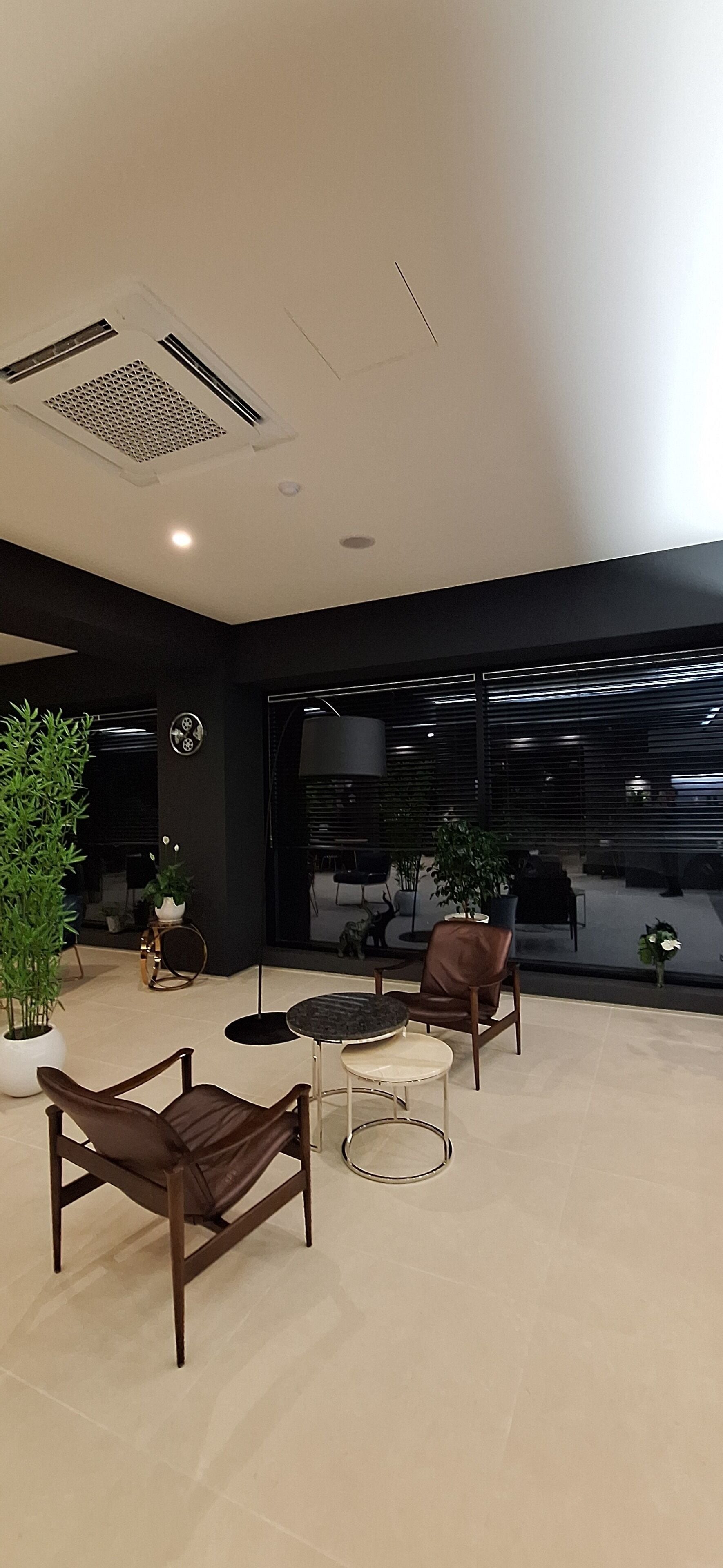 Um interior moderno com área de estar, plantas em vasos e vista através de grandes janelas.