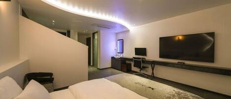 Habitación de hotel moderna con techo curvo, una cama grande, un escritorio con computadora, televisor de pantalla plana y un ventanal amplio.