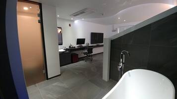 Un baño moderno con una bañera blanca, un escritorio con un ordenador y un televisor de pantalla plana.