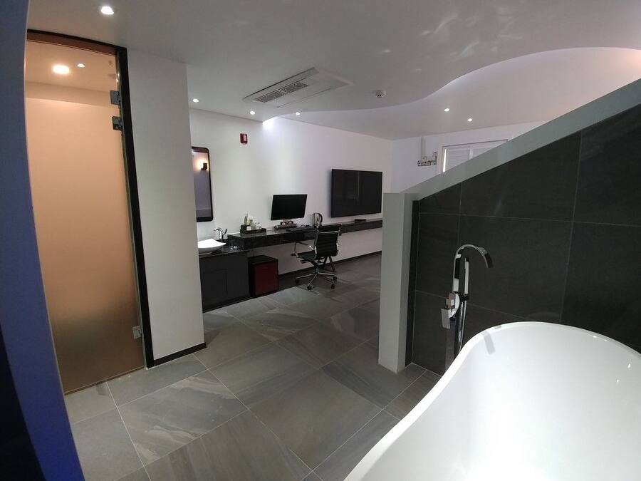 Un baño moderno con una bañera blanca, un escritorio con un ordenador y un televisor de pantalla plana.