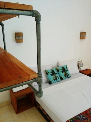 A room with a bed, a wooden table, and two wall-mounted lamps.