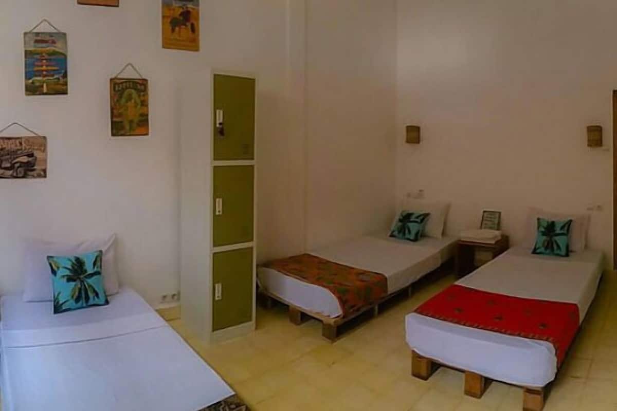 Quarto com três camas individuais, cada uma com travesseiro e cobertor. Há decorações nas paredes e um armário verde.