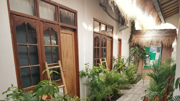 Un pasillo al aire libre cubierto con piso de baldosas, rodeado de exuberantes plantas verdes y puertas de madera.