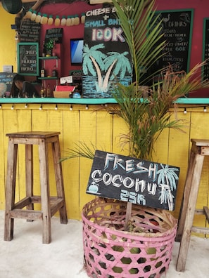 A bar with a chalkboard menu, stools, and a sign for fresh coconut juice.