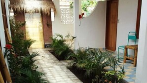 Un sendero estrecho con piso de baldosas, bordeado por plantas en macetas y una estructura de techo de paja.