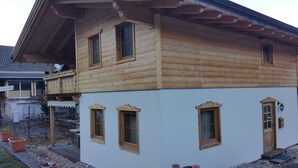 Una casa de madera de dos pisos con un balcón, varias ventanas y un porche con una puerta.