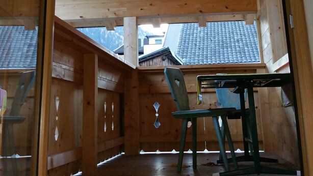 Interior de madera con techo alto, una lámpara redonda en el techo y vista al exterior a través de una puerta de cristal.