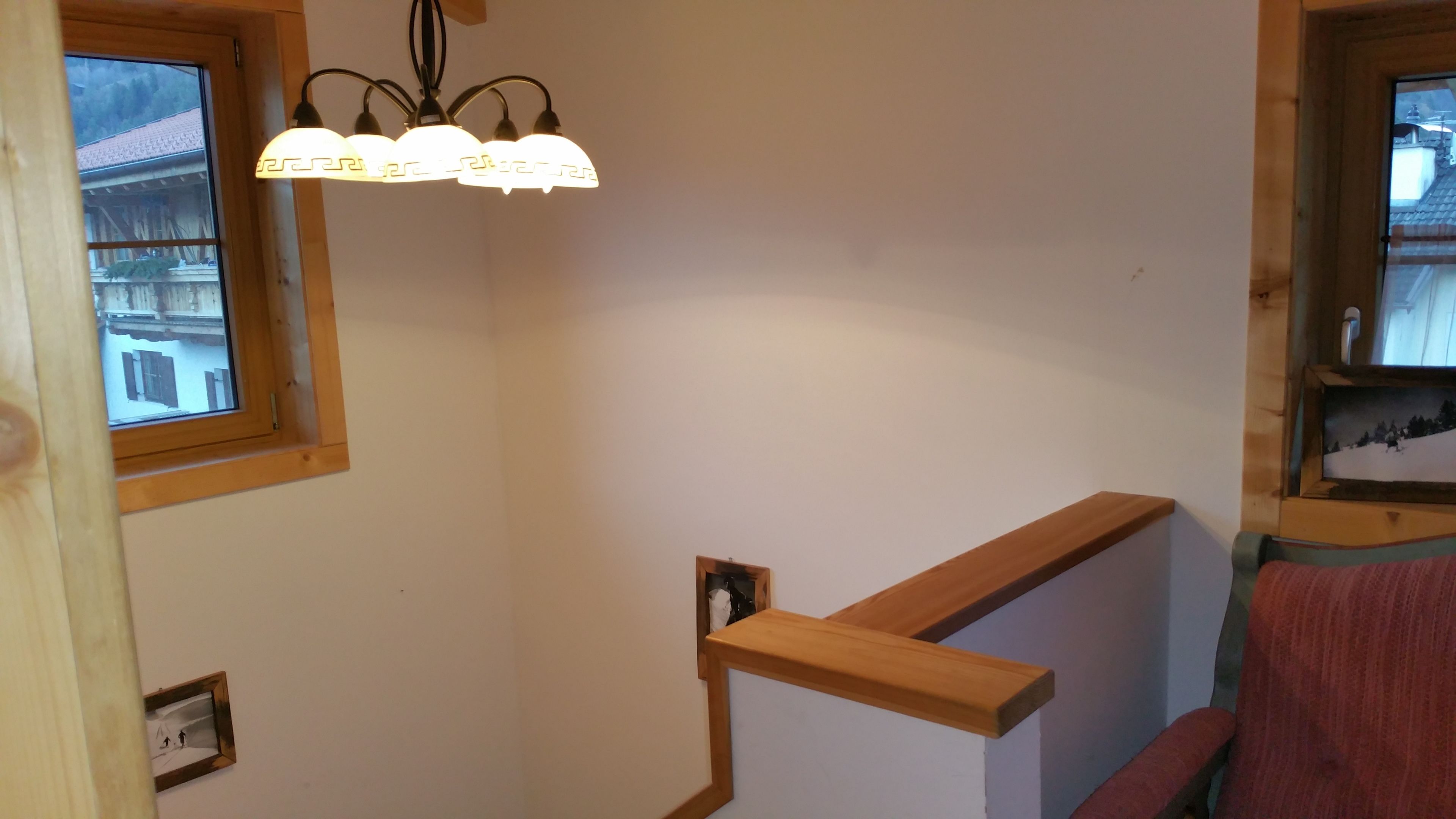 A staircase with wooden handrails, a wall-mounted light fixture, and a window with a view of a building.
