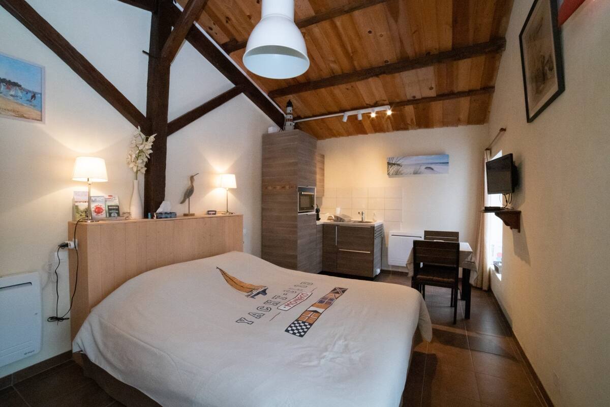 Une chambre dotée d’un grand lit, de poutres apparentes en bois au plafond, d’une petite kitchenette et d’un coin repas.