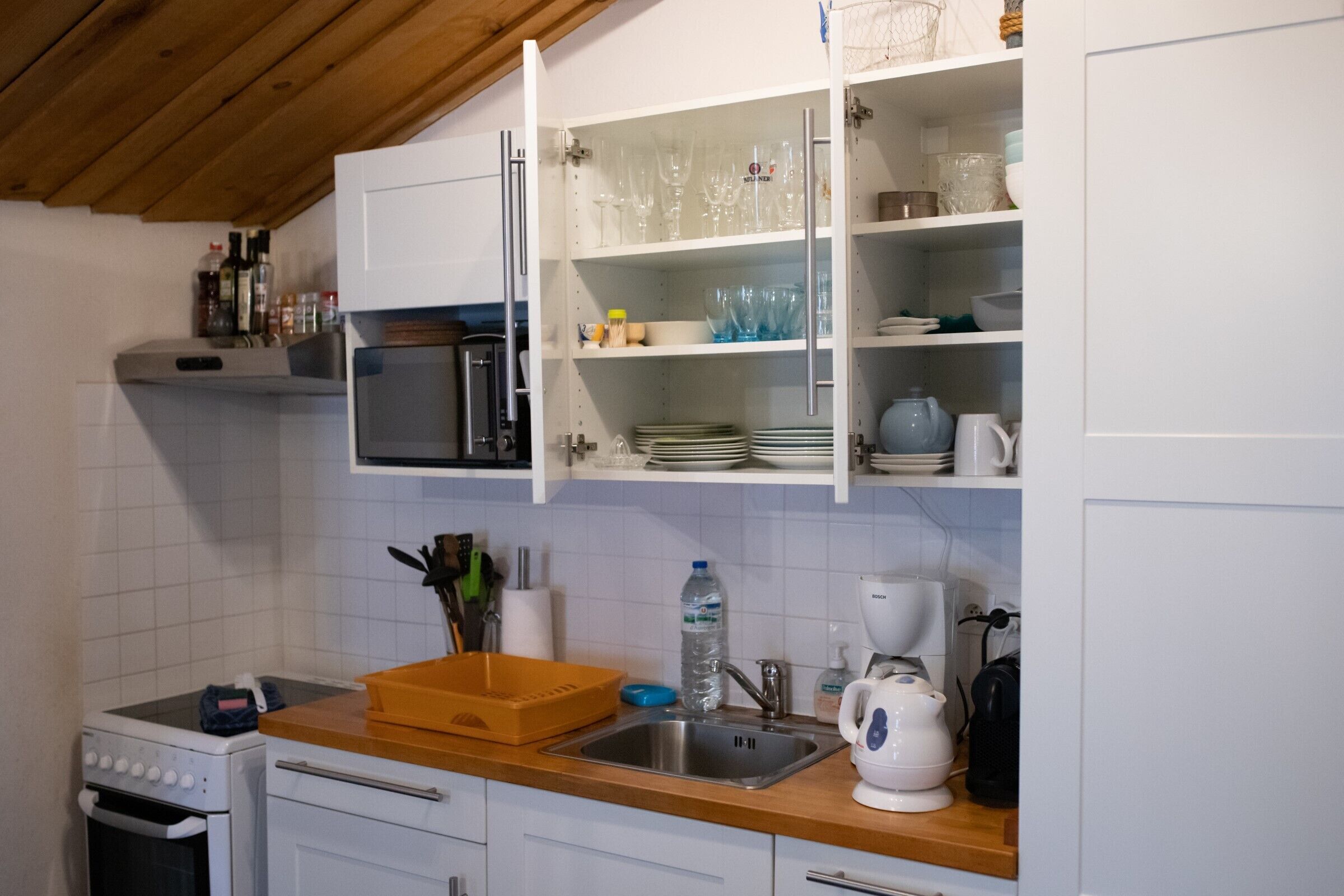 Una cocina con armarios blancos, microondas, pileta y cafetera.