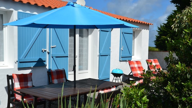 Een terras met een tafel, stoelen, een blauwe parasol en een barbecue.