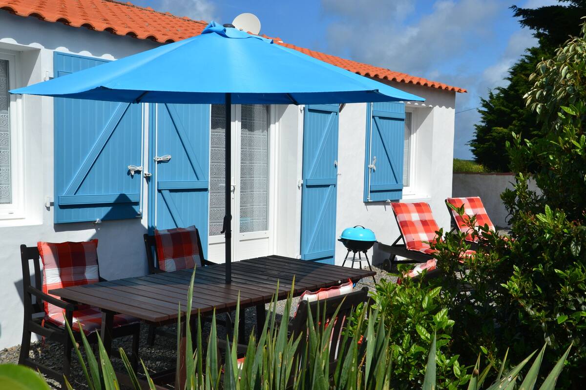 Une terrasse avec une table et des chaises, un parasol bleu et un barbecue.