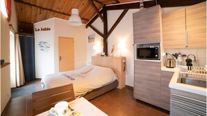 Een kleine kamer met een bed, kitchenette en een eethoek.