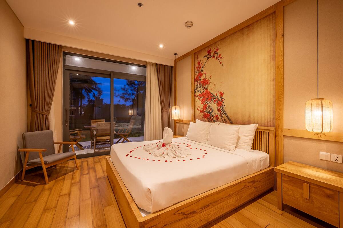 Ein Hotelzimmer mit einem großen Bett, Holzboden, Blick durch die Glastür und einem traditionellen Kunstwerk an der Wand.