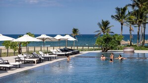 Ein Poolbereich mit Liegestühlen und Sonnenschirmen, eine Palme und Meerblick.