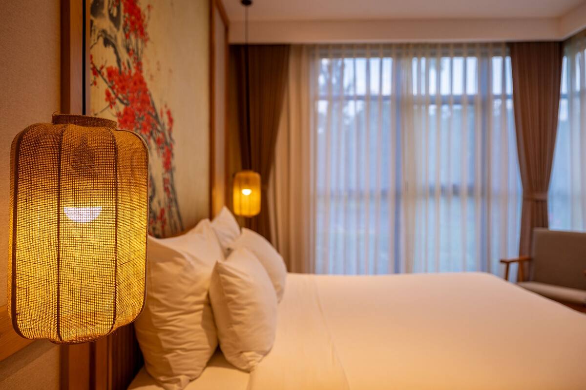 Ein Hotelzimmer mit einem Bett, Kissen, einer Wandlampe und einem Gemälde.