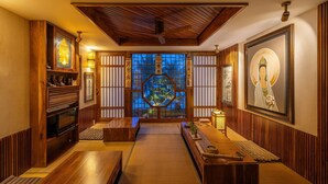 Ein traditioneller japanischer Raum mit Tatami-Böden, einer niedrigen Holzbalkendecke und Blick auf einen Baum durch einen Shoji-Bildschirm.