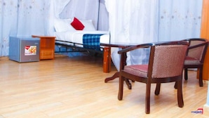 A room with a bed under a canopy, a small table, two chairs, and a suitcase. - Babblers Park (Migori)