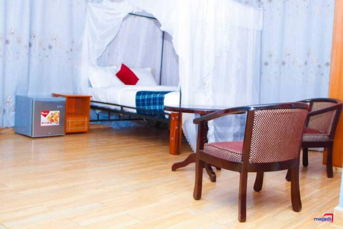 A room with a bed under a canopy, a small table, two chairs, and a suitcase.