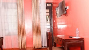 A room with a wooden desk, a chair, a television mounted on the wall, and a water bottle on the desk. - Babblers Park (Migori)
