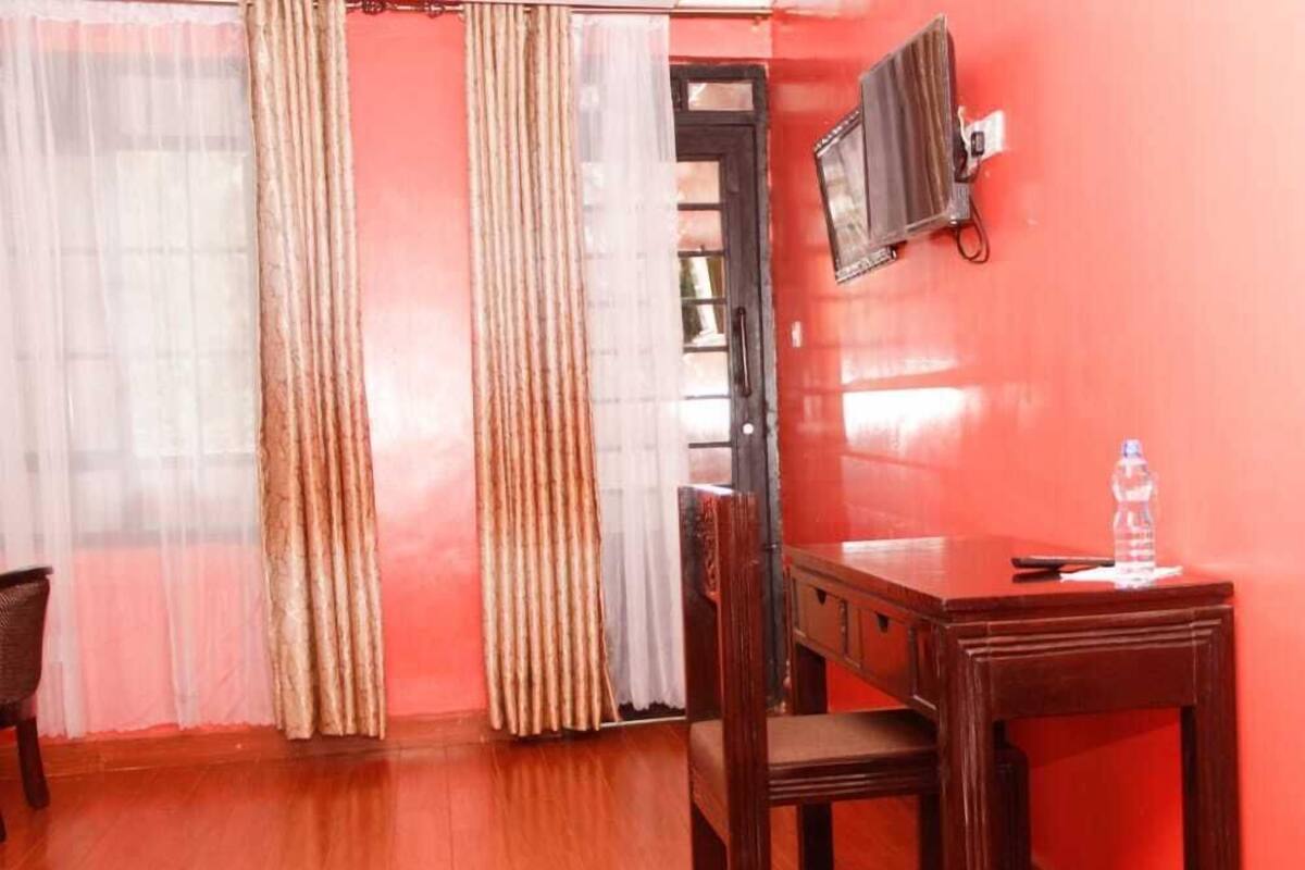 A room with a wooden desk, a chair, a television mounted on the wall, and a water bottle on the desk.